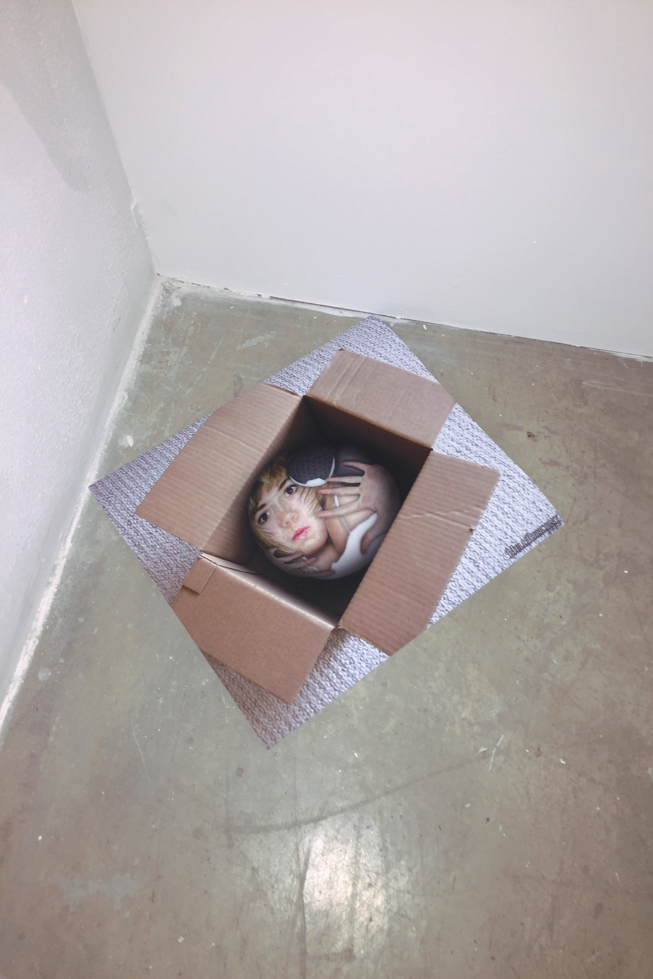 Small print on the floor of a girl stylistically stuffed into a cardboard box